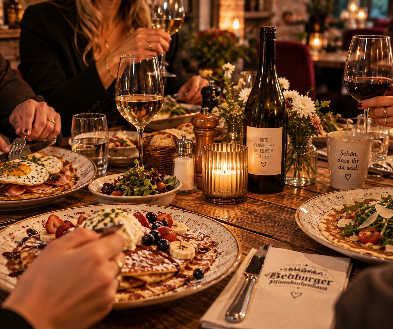 Gedeckter Tisch mit Pfannkuchen, Händen, Besteck, Wein und Wasser im warmen Restaurantlicht